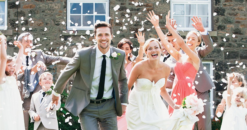 a newly married couple with beautiful smiles running through a crowd of guests who are throwing flower petals