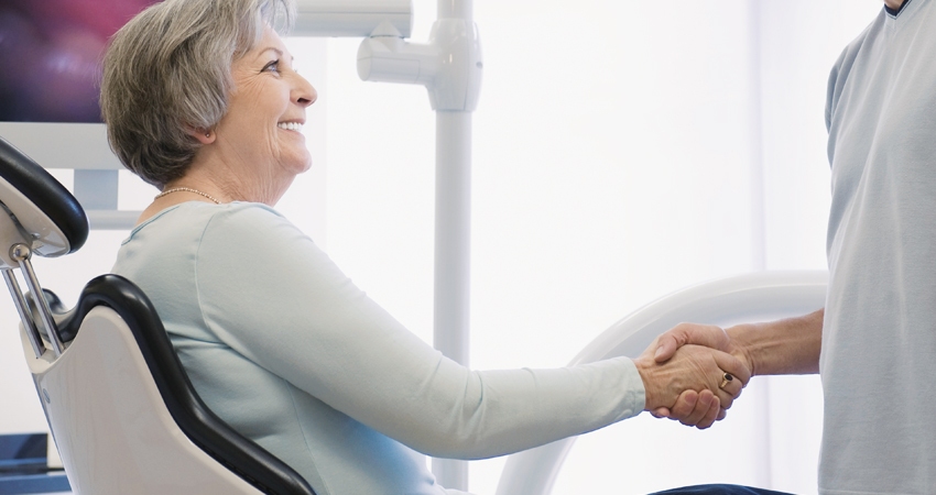 older woman sitting in a dental chair and shaking hands with her new dentist in Batavia